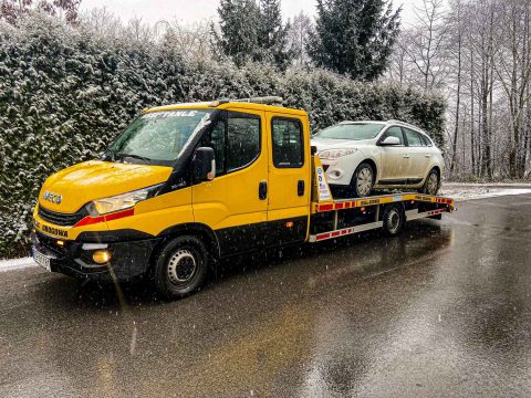 Żółta laweta Iveco transportuje samochód osobowy zimą